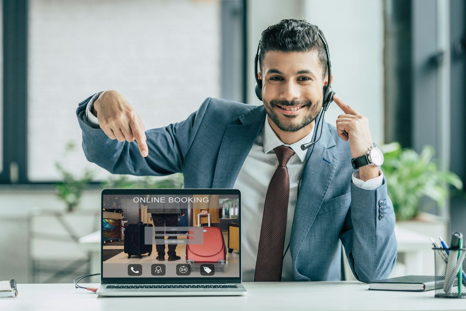 cheerful call center operator pointing with finger at laptop with online booking website on screen