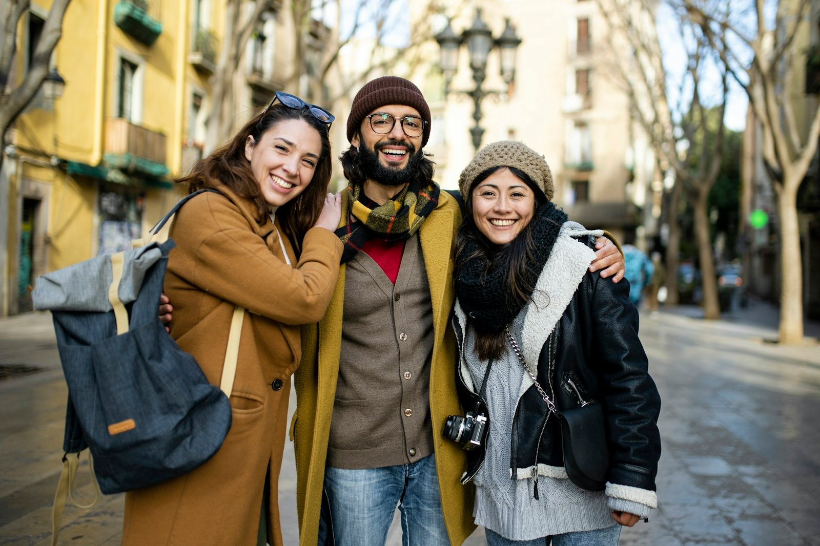 Portrait of three happy tourists standing on the street and looking at camera. Group of travelers